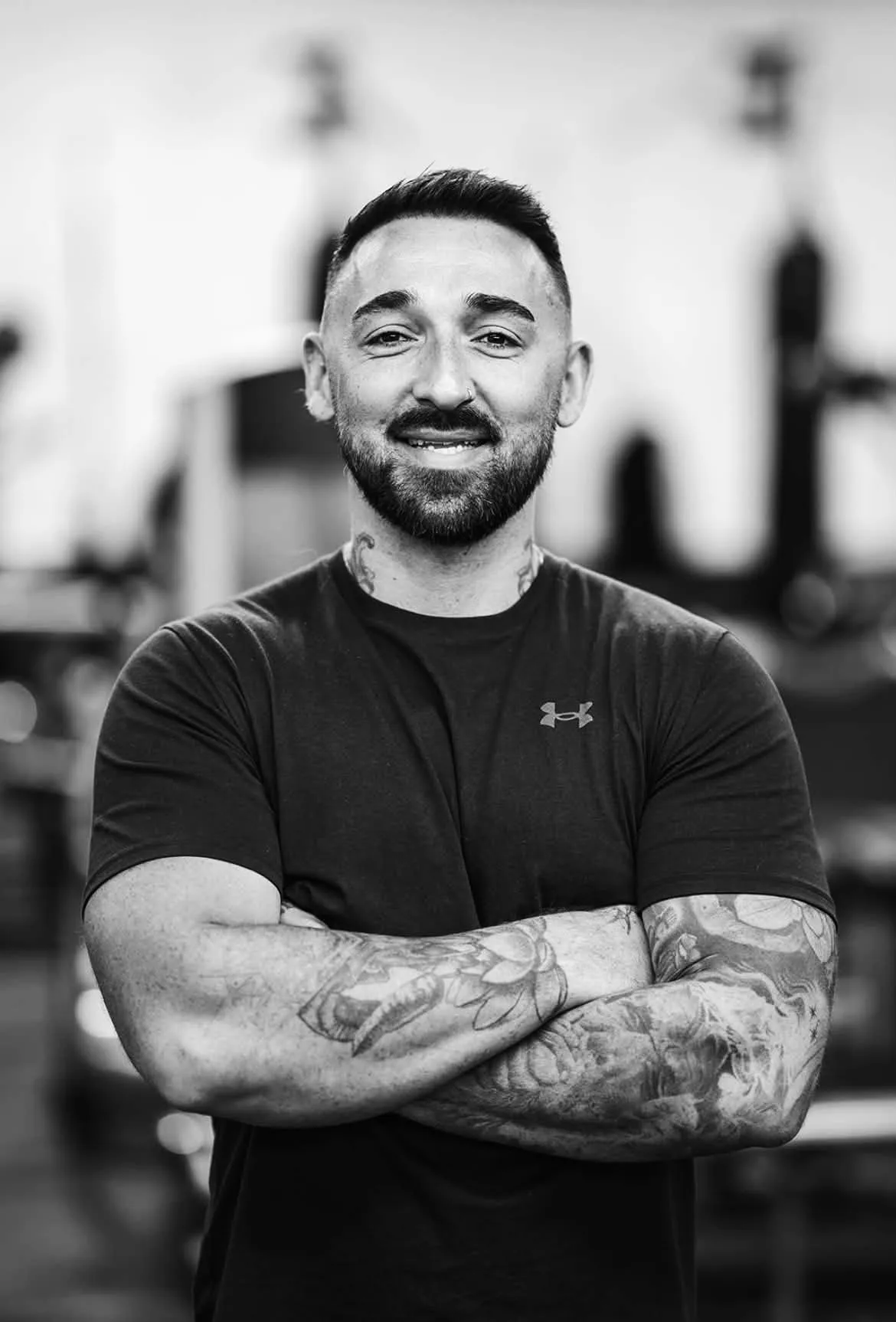 Gareth Mackay, owner of Transpire, smiling with his arms crossed in a black T-shirt on the gym floor.
